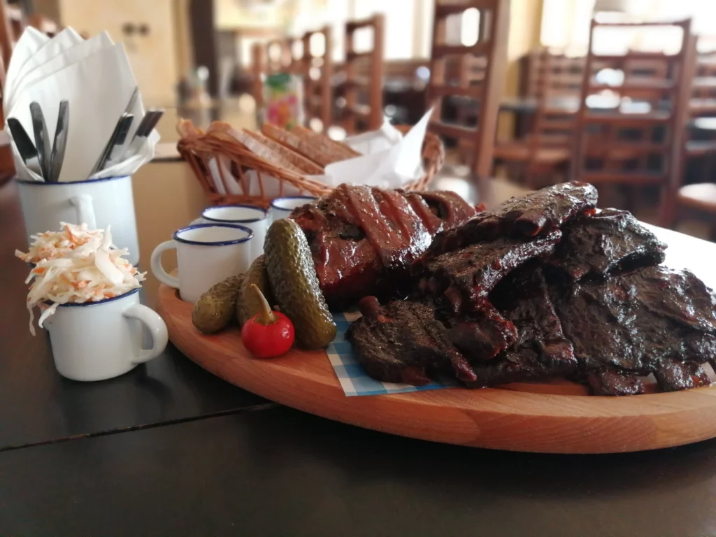 Fotografie menu pečeného vepřového kolene s vepřovými žebry ustavené na dřevěné prkénko položené na stole.