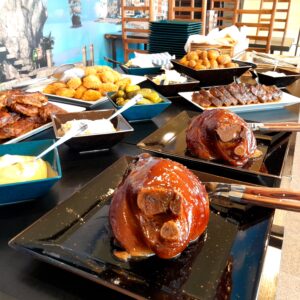 Rautový stůl plný jídla: pečené zauzené vepřové koleno, vepřová žebra BBQ, řízečky, vepřová krkovička, pečené brambory.